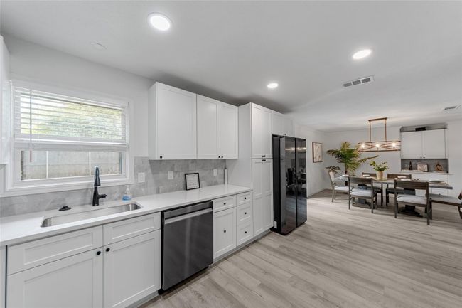 Kitchen with tasteful backsplash, light wood finished floors, stainless steel dishwasher, white cabinets, and fridge with ice dispenser | Image 8
