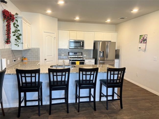 Kitchen with appliances with stainless steel finishes, a sink, a peninsula, white cabinetry, and dark wood finished floors | Image 9