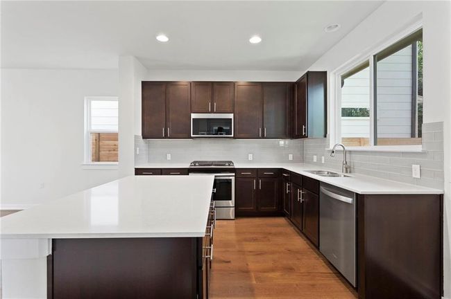 Kitchen with stainless steel appliances, light countertops, dark brown cabinetry, light wood-type flooring, and recessed lighting | Image 5