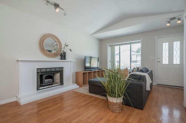 Living room with wood finished floors, a fireplace, visible vents, a notable chandelier, and lofted ceiling | Image 4