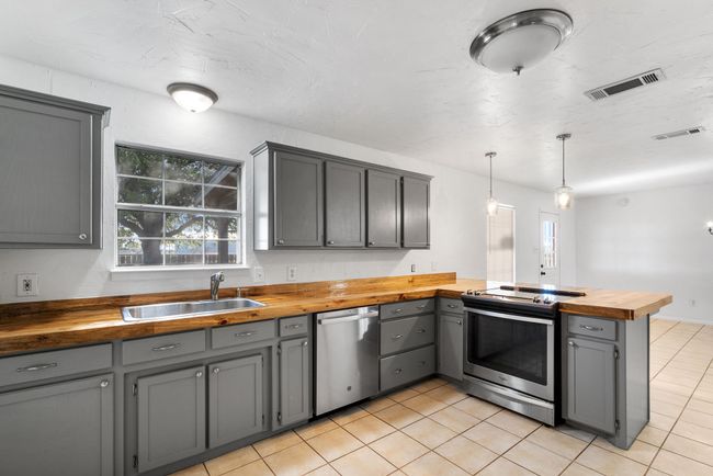 Kitchen with wood counters, stainless steel appliances, gray cabinets, a peninsula, and light tile patterned floors | Image 6