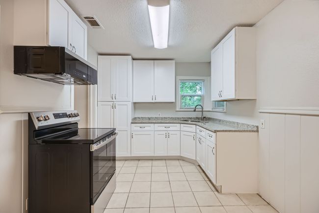 Kitchen with white cabinetry, light tile patterned floors, stainless steel electric range oven, and a sink | Image 11