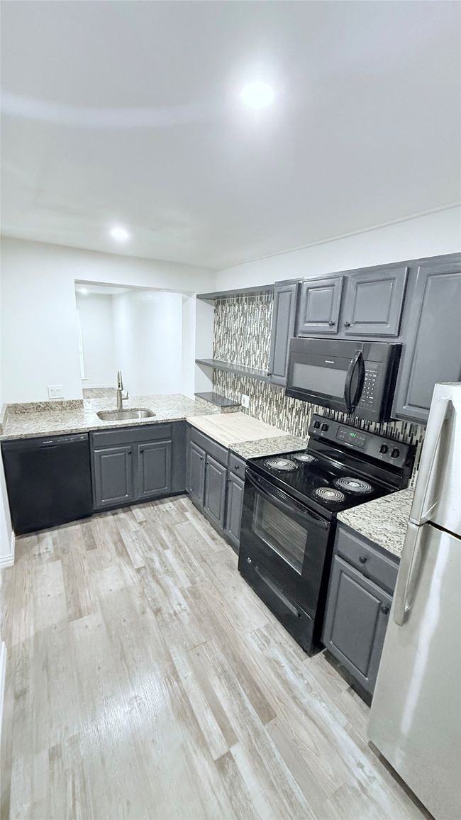 Kitchen featuring black appliances, gray cabinets, a sink, light wood-style floors, and light stone counters | Image 7