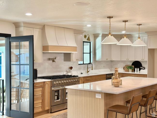 Kitchen with premium range hood, double oven range, decorative backsplash, light stone counters, and dishwashing machine | Image 11