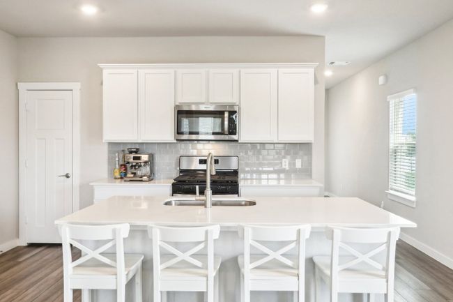 Kitchen with a sink, stainless steel appliances, white cabinetry, tasteful backsplash, and dark wood-style vinyl flooring | Image 9
