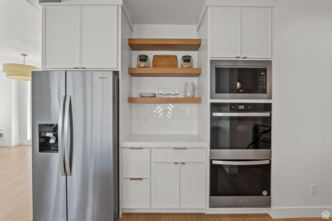 Kitchen featuring white cabinets, stainless steel appliances, tasteful backsplash, open shelves, and light stone countertops | Image 21