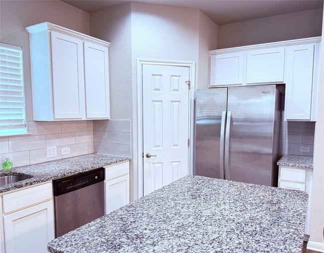 Kitchen with stainless steel appliances, backsplash, light stone countertops, and white cabinets | Image 5