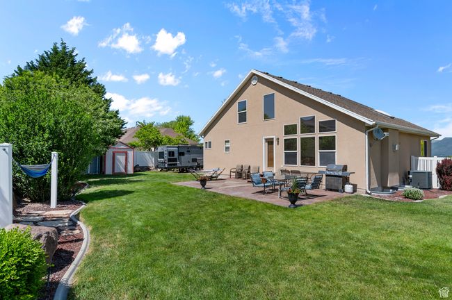 Back of property with stucco siding, a patio, central AC, and a lawn | Image 25