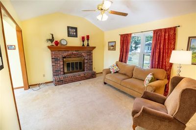 Carpeted living room featuring vaulted ceiling, ceiling fan, and a brick fireplace | Image 3