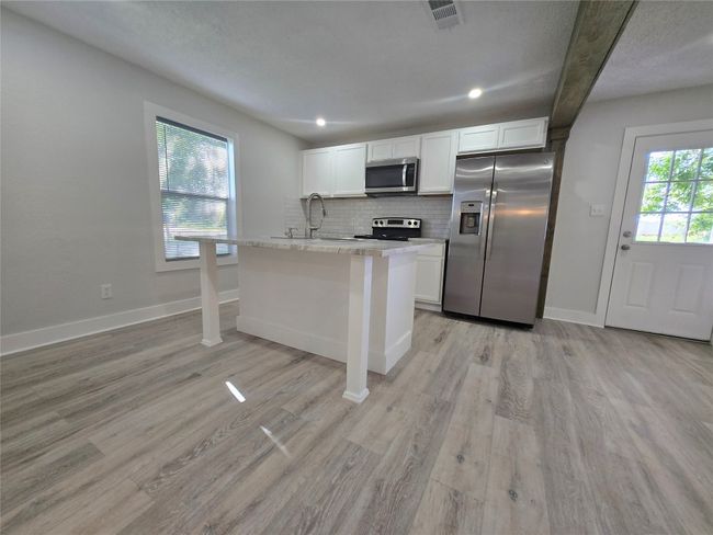 Kitchen with stainless steel appliances, white cabinets, light countertops, light wood finished floors, and backsplash | Image 8