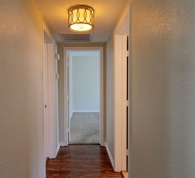 Hall with a textured wall, visible vents, baseboards, and wood finished floors | Image 14