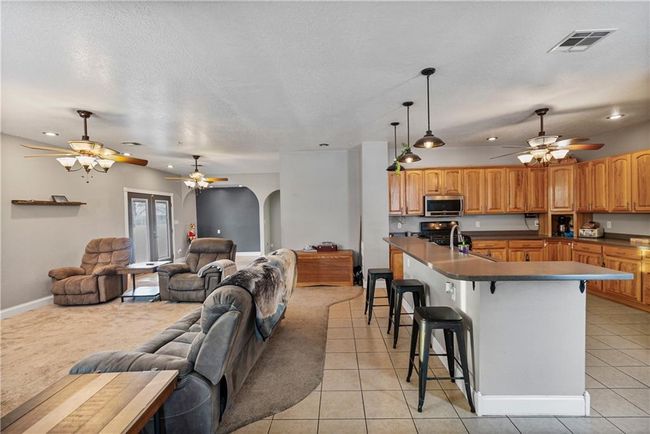 Kitchen featuring light tile patterned flooring, decorative light fixtures, a breakfast bar area, a center island with sink, and a textured ceiling | Image 12