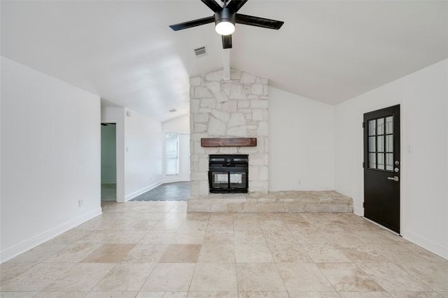Unfurnished living room featuring visible vents, a ceiling fan, baseboards, a stone fireplace, and vaulted ceiling with beams | Image 6