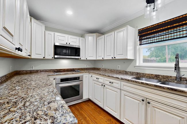 Kitchen with appliances with stainless steel finishes, ornamental molding, white cabinetry, light wood-type flooring, and stone counters | Image 11
