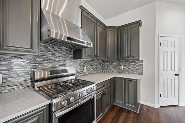 Kitchen featuring stainless steel gas range oven, wall chimney exhaust hood, dark wood-style floors, and tasteful backsplash | Image 10