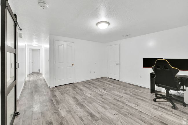 Office space with a textured ceiling, visible vents, light wood finished floors, baseboards, and a barn door | Image 26