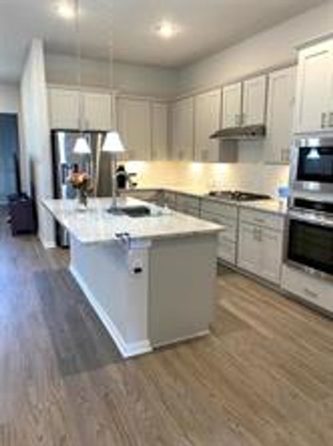Kitchen with gas stovetop, dark wood-style flooring, light countertops, and a center island with sink | Image 6