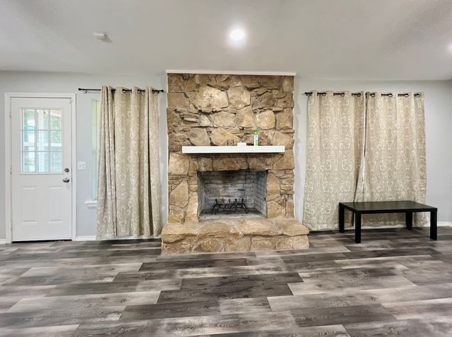 Unfurnished living room featuring wood finished floors and a stone fireplace | Image 5
