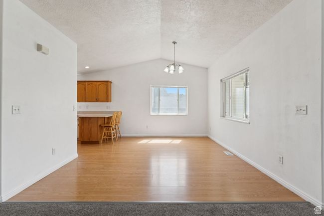 Unfurnished living room with lofted ceiling, light wood-style floors, a chandelier, and a textured ceiling | Image 4