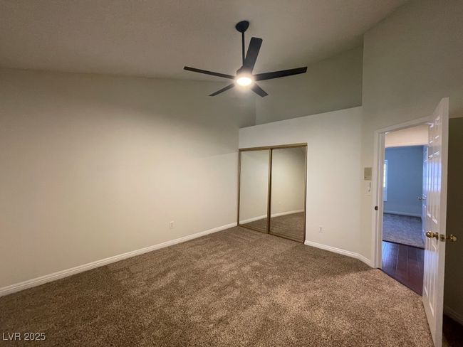 Unfurnished bedroom with dark colored carpet, high vaulted ceiling, a closet, and ceiling fan | Image 19