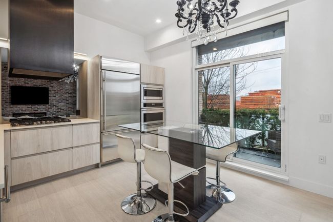 Kitchen featuring light brown cabinets, wall chimney exhaust hood, built in appliances, and a notable chandelier | Image 7