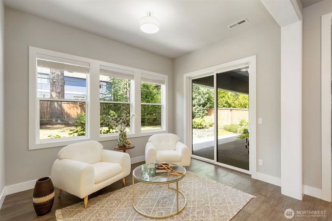Just off the open-concept kitchen, this light-filled sitting room offers a cozy spot for morning coffee or casual conversation. Large windows and sliding glass doors frame the lush backyard, blending indoor comfort with outdoor serenity. | Image 11