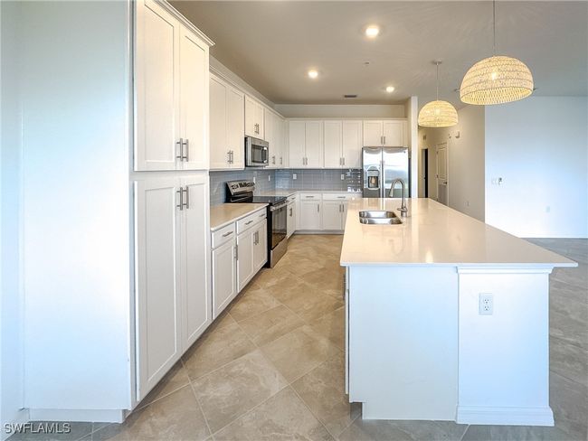 Kitchen featuring appliances with stainless steel finishes, a sink, a kitchen island with sink, tasteful backsplash, and white cabinets | Image 7