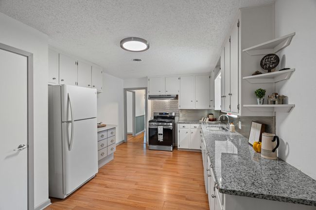 Kitchen with freestanding refrigerator, stainless steel gas stove, under cabinet range hood, open shelves, and light wood finished floors | Image 10