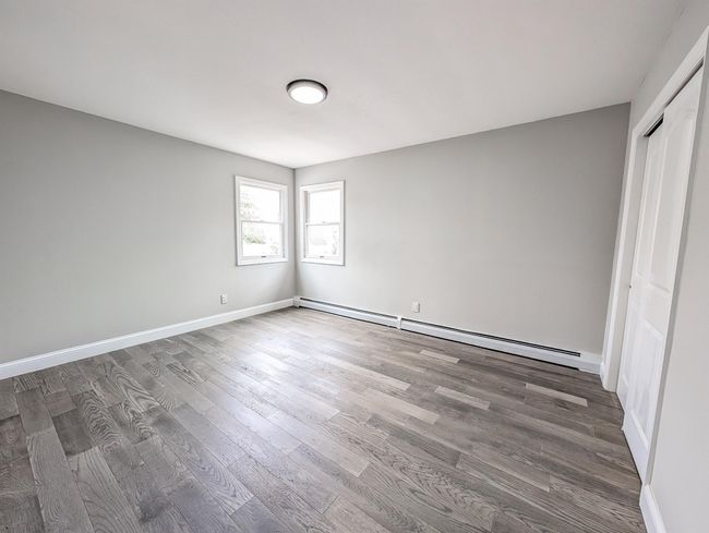 Unfurnished bedroom with a baseboard radiator, a closet, baseboards, and wood finished floors | Image 10