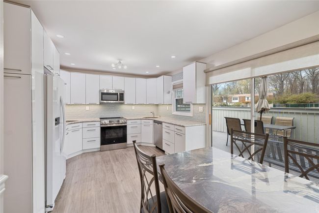 Kitchen featuring stainless steel appliances, light wood-style floors, white cabinetry, decorative backsplash, and light stone countertops | Image 13