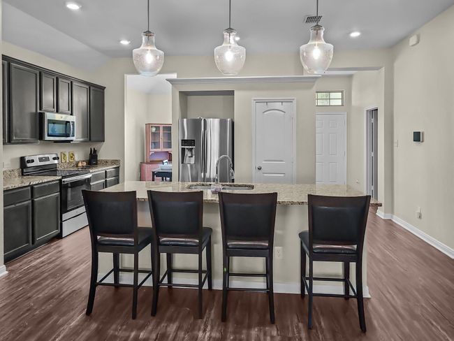 Kitchen with stainless steel appliances, dark wood-type flooring, light stone counters, a kitchen bar, and recessed lighting | Image 7