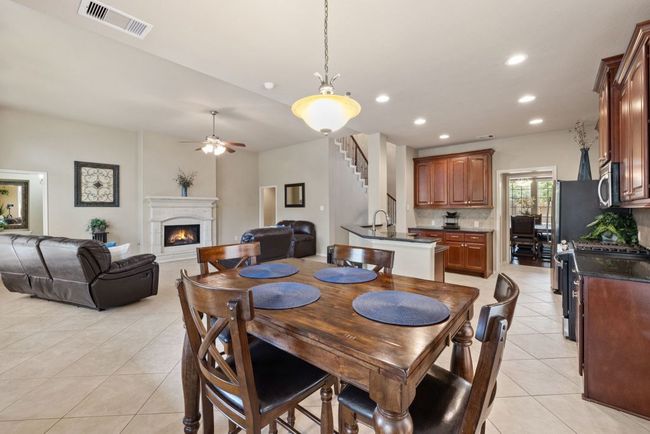 Dining room featuring light tile patterned flooring, a lit fireplace, a ceiling fan, stairs, and recessed lighting | Image 14
