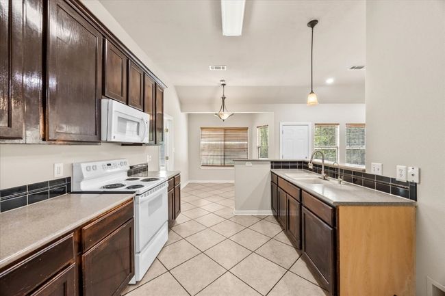 Kitchen with white appliances, visible vents, a sink, and dark brown cabinets | Image 13
