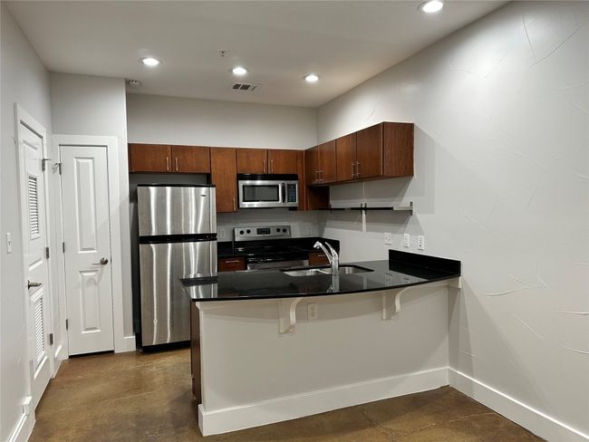 Kitchen with appliances with stainless steel finishes, a peninsula, dark countertops, recessed lighting, and a breakfast bar area | Image 13