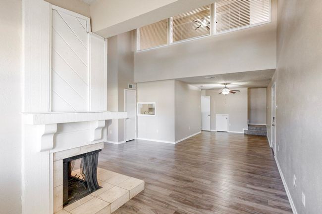 Unfurnished living room with baseboards, ceiling fan, a tile fireplace, a towering ceiling, and wood finished floors | Image 9