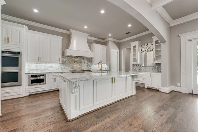 Kitchen with glass insert cabinets, double oven, custom range hood, dark wood finished floors, and white cabinetry | Image 12