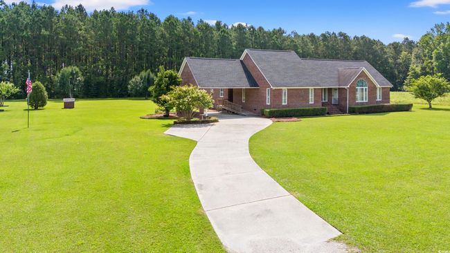 View of front of home featuring concrete driveway, a front lawn, brick siding, a forest view, and roof with shingles | Image 23