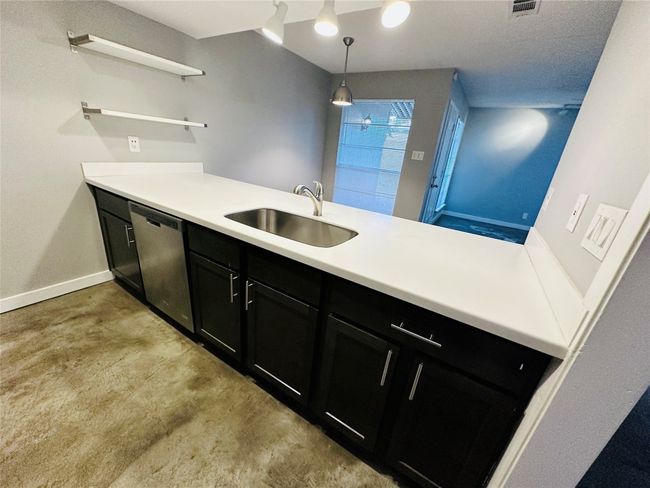 Kitchen with dishwasher, a peninsula, concrete floors, open shelves, and light countertops | Image 4
