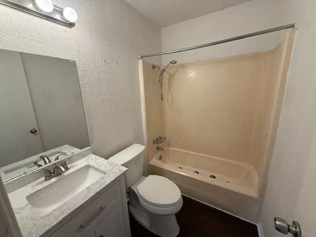 Bathroom featuring a textured wall, bathtub / shower combination, a textured ceiling, vanity, and wood finished floors | Image 12