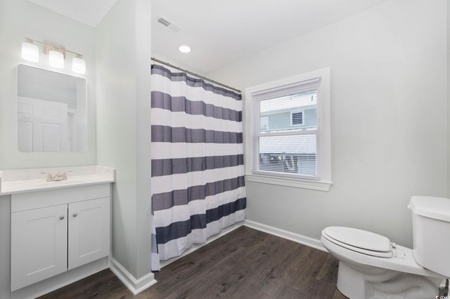 Bathroom featuring toilet, vanity, baseboards, wood finished floors, and curtained shower | Image 21