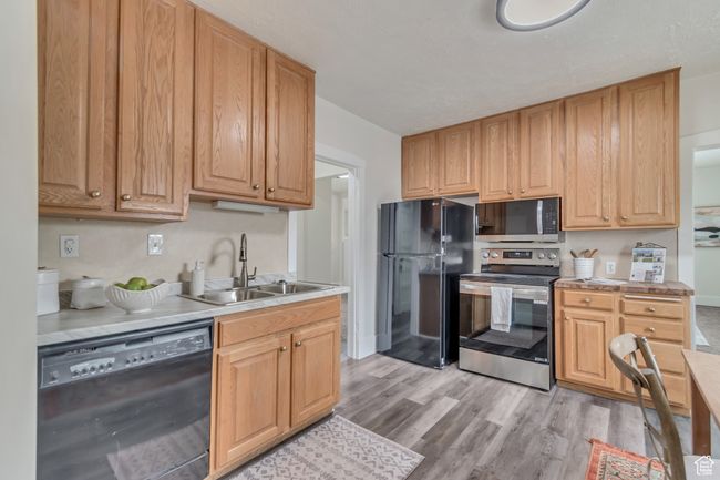 Kitchen featuring a sink, light wood-style floors, black appliances, and light countertops | Image 10