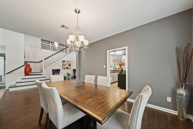 This elegant dining room features rich wood flooring, designer gray paint, and a chic chandelier that sets the tone for everything from festive holiday dinners to casual family meals. | Image 11