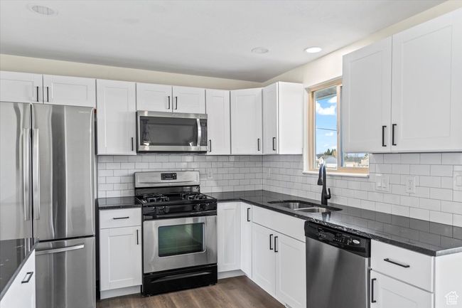 Kitchen featuring a sink, appliances with stainless steel finishes, dark wood-style floors, white cabinets, and dark stone counters | Image 9