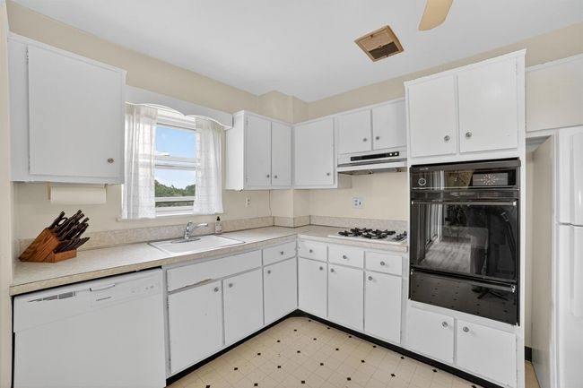 Kitchen with white appliances, a warming drawer, under cabinet range hood, white cabinetry, and light countertops | Image 20