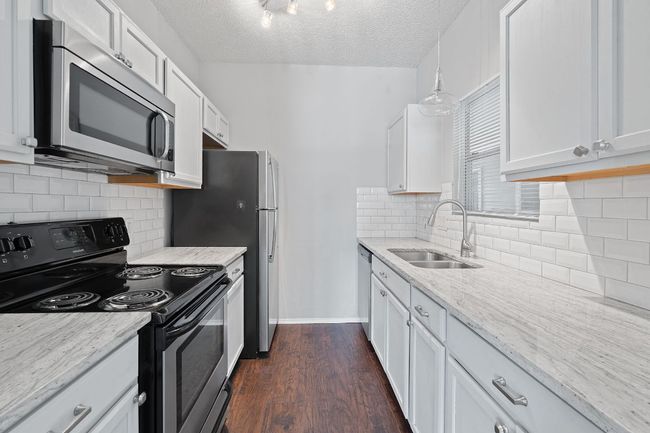 Kitchen with a sink, a textured ceiling, light stone counters, white cabinets, and appliances with stainless steel finishes | Image 6