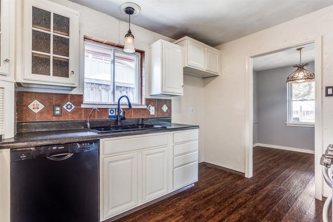 Kitchen with black dishwasher, a sink, dark countertops, dark wood-style floors, and white cabinetry | Image 14