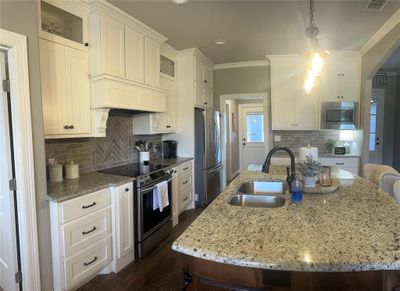 Kitchen with dark hardwood / wood-look tile flooring, pendant lighting, appliances with stainless steel finishes, sink, and white custom cabinetry | Image 2