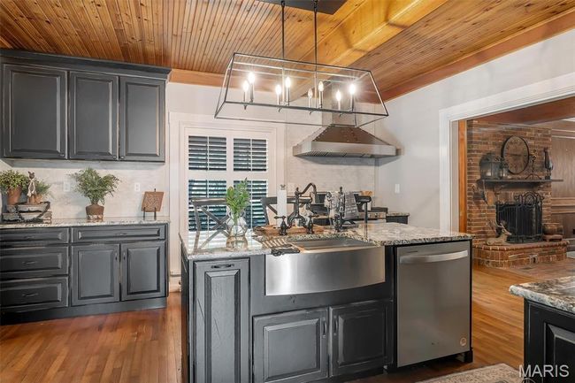 Kitchen with dishwasher, wooden ceiling, wall chimney exhaust hood, dark wood-style flooring, and light stone countertops | Image 45