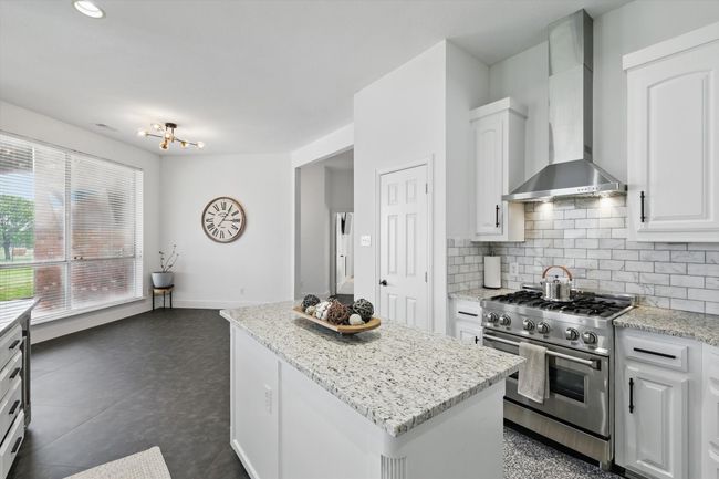 Large kitchen island with propane gas powered stove, and contemporary vent hood. | Image 15