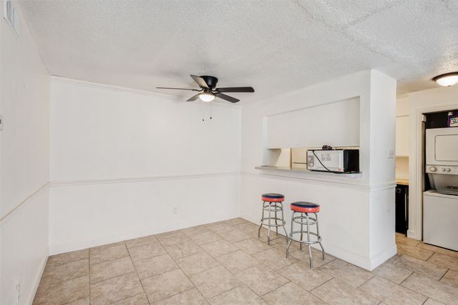 Kitchen featuring a breakfast bar area, white microwave, visible vents, a textured ceiling, and stacked washer / dryer | Image 10